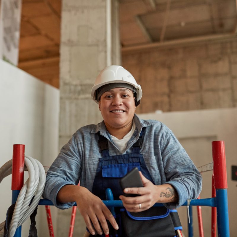 Portrait of mixed-race female worker wearing hardhat and smiling at camera while enjoying work on construction site, copy space